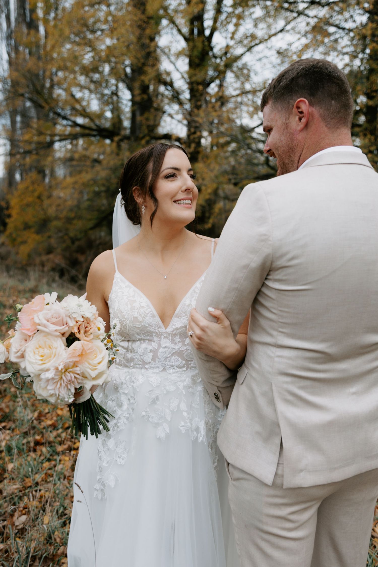 A bride and groom embracing with the Autumn trees in the background