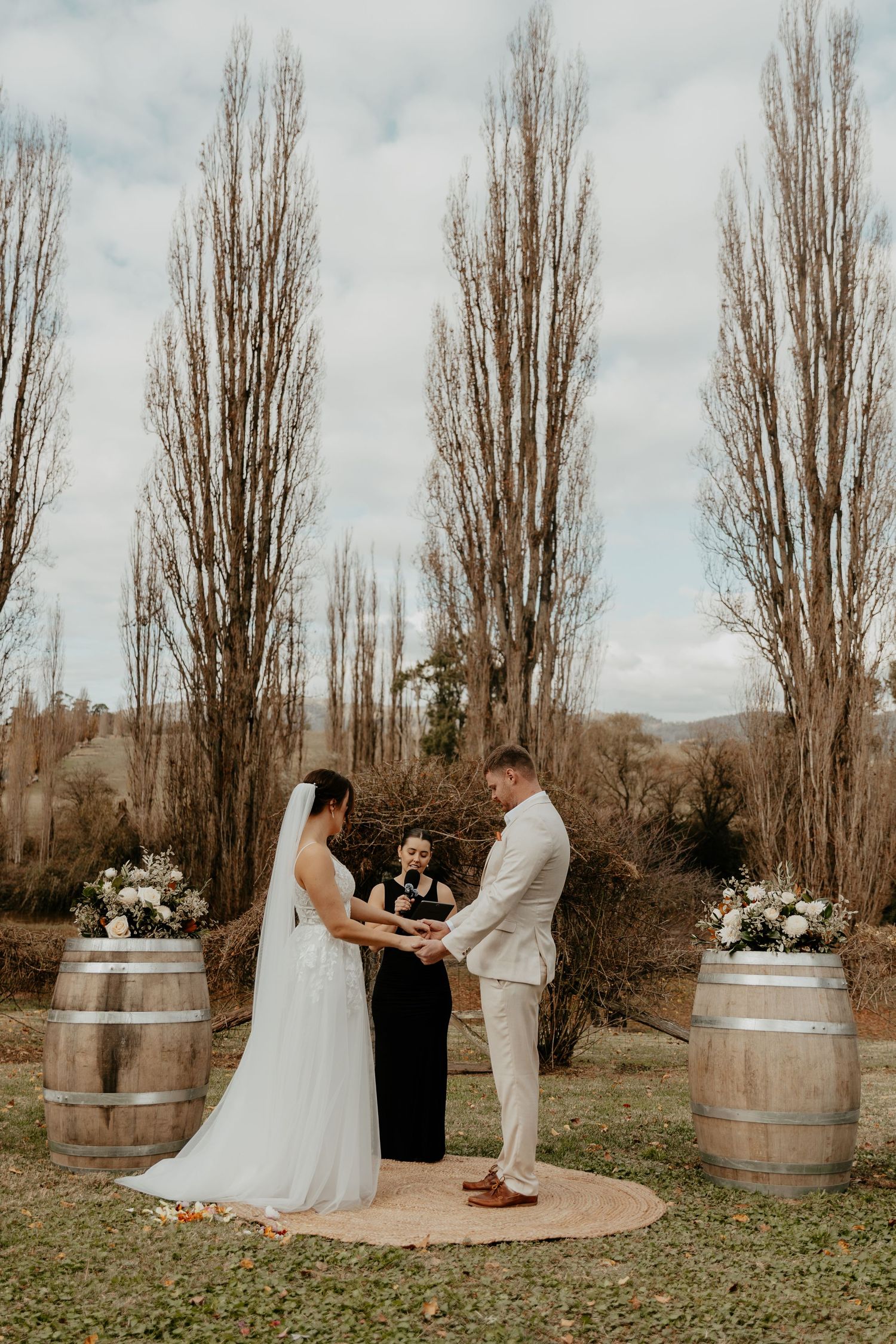 A bride and groom at their outdoor wedding ceremony holding hands while the celebrant takes them through their vowels