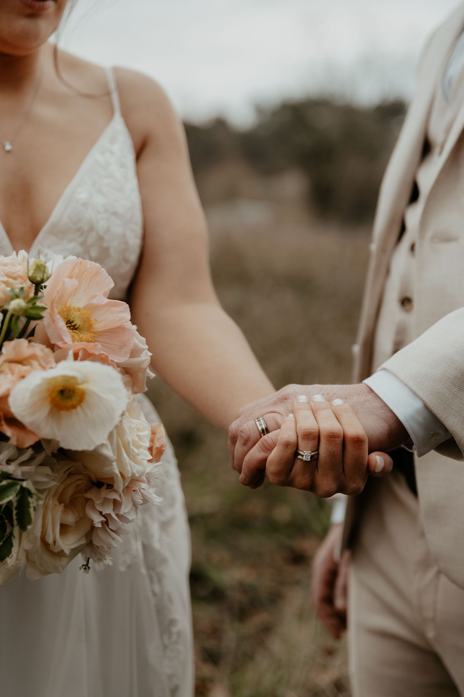 A bridal couple holding hands after the ceremony with the rings visible and the bride's bouquet and dress featured
