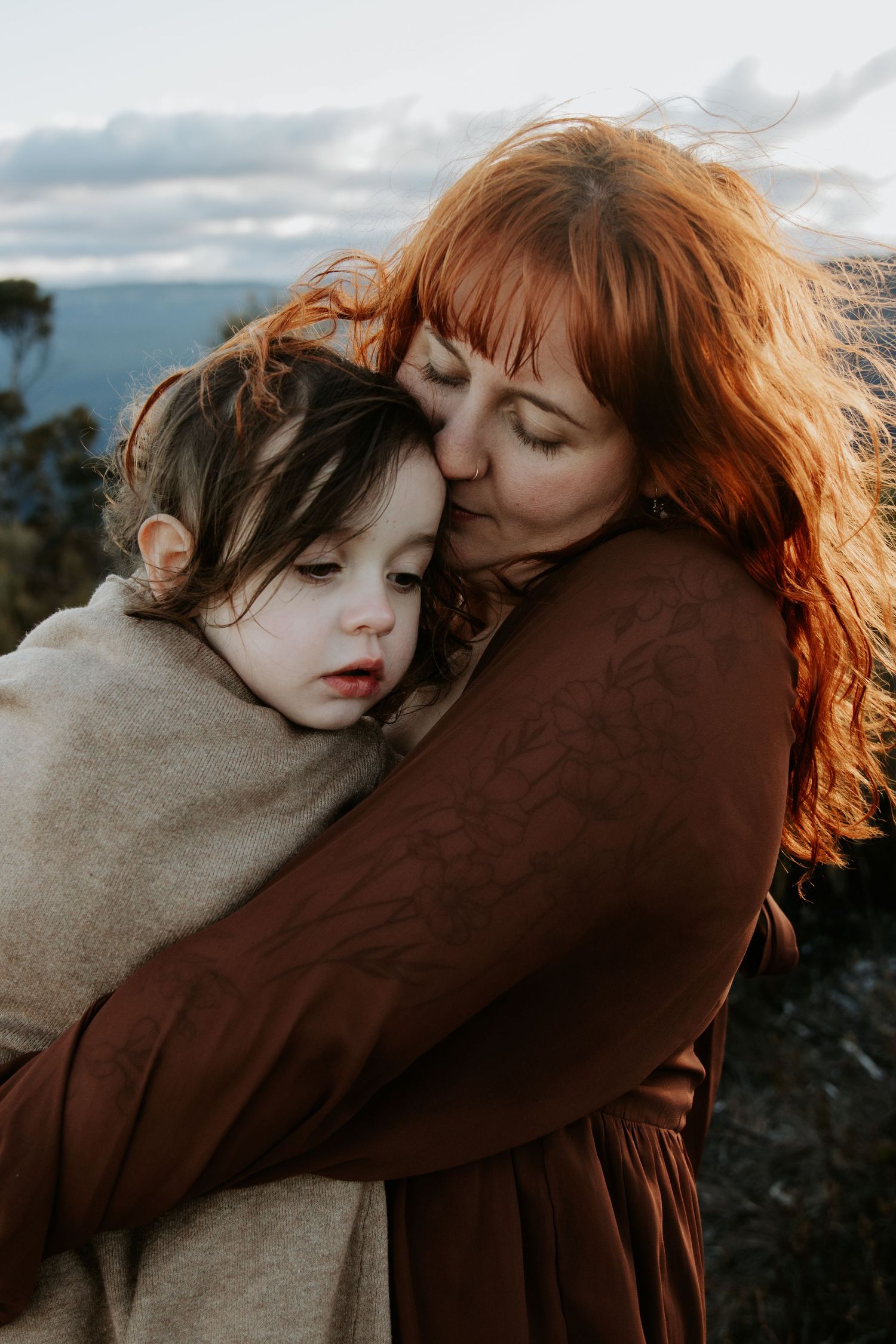 A mother embracing her child wrapping her up in a blanket to protect her from the cold wind
