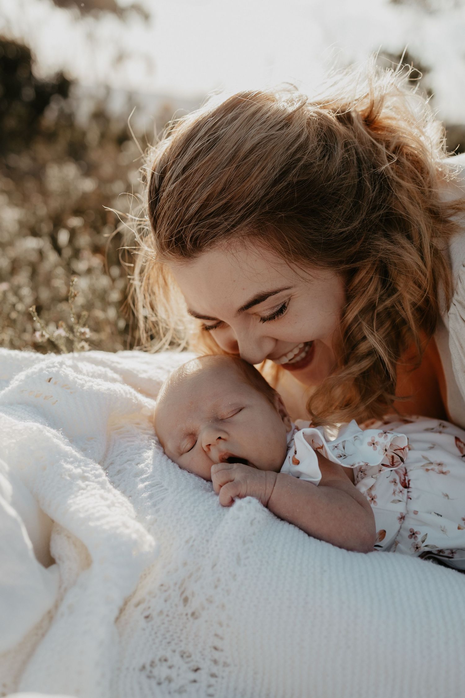 A mother smiling at her baby lying on the blanket amongst the wildflowers