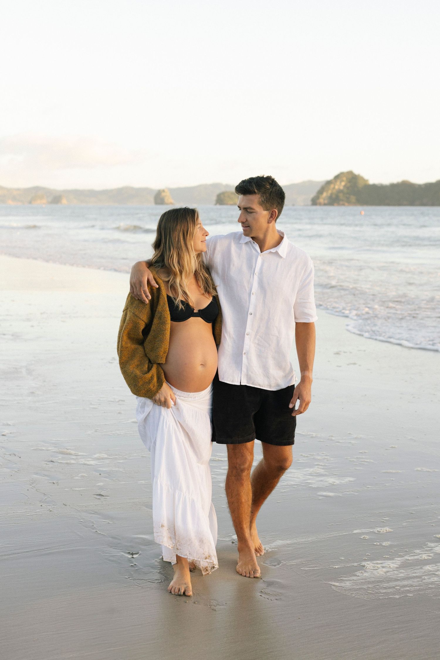 Couple embrace during maternity photoshoot on beach