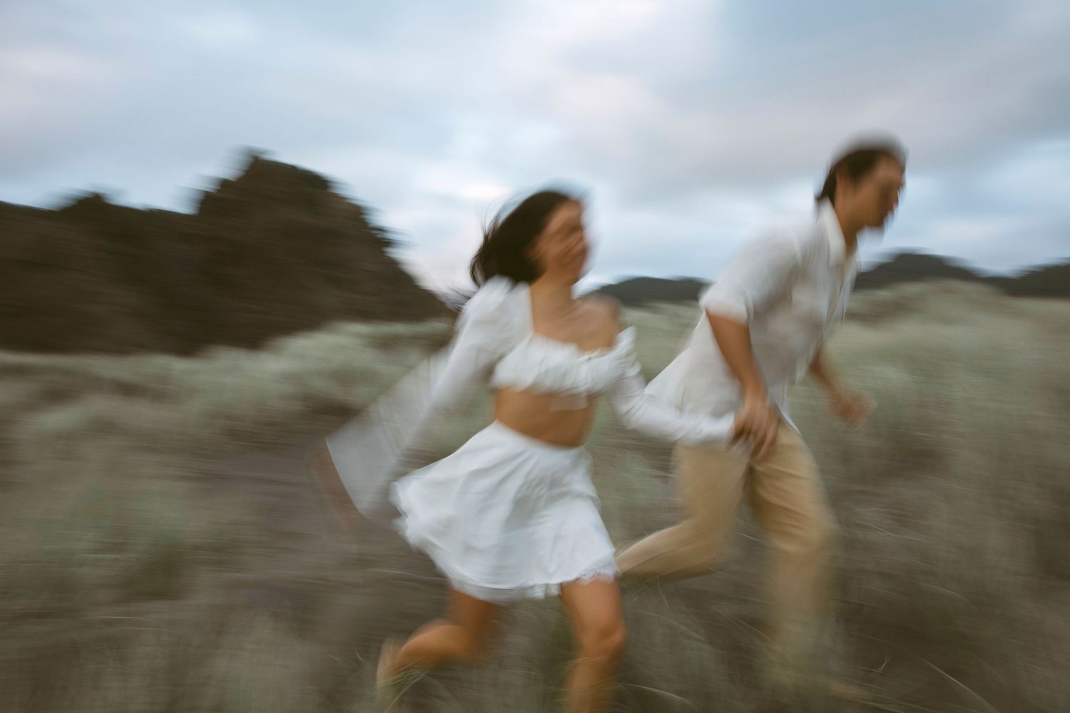 Blurred engaged couple running across dunes