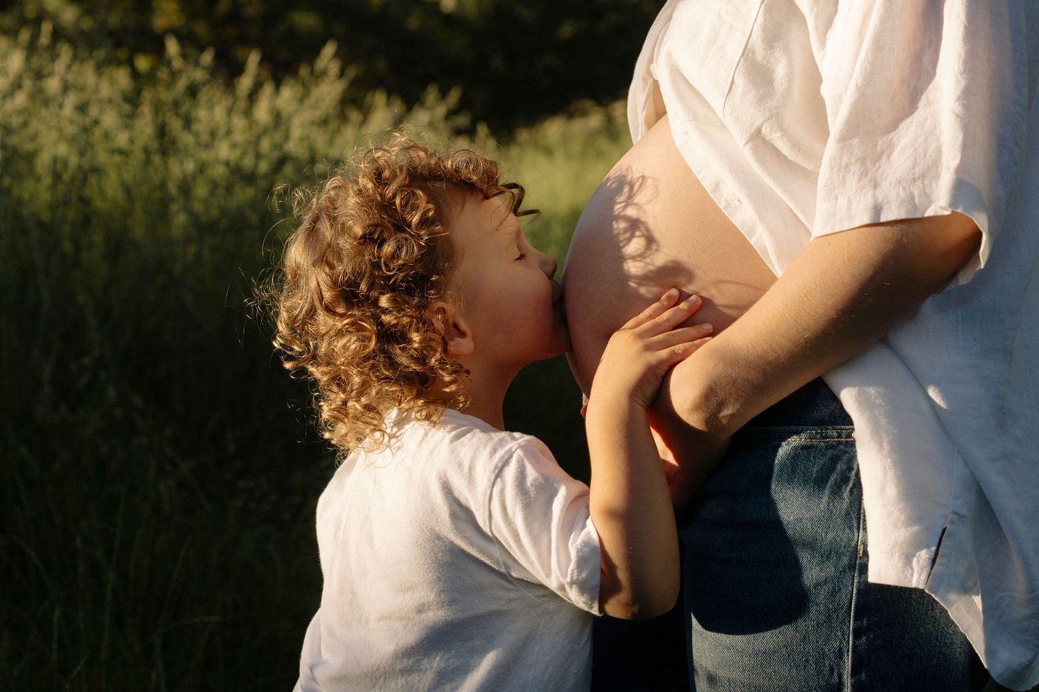 Toddler kissing mums pregnant stomach during family photoshoot in Cornwall Park