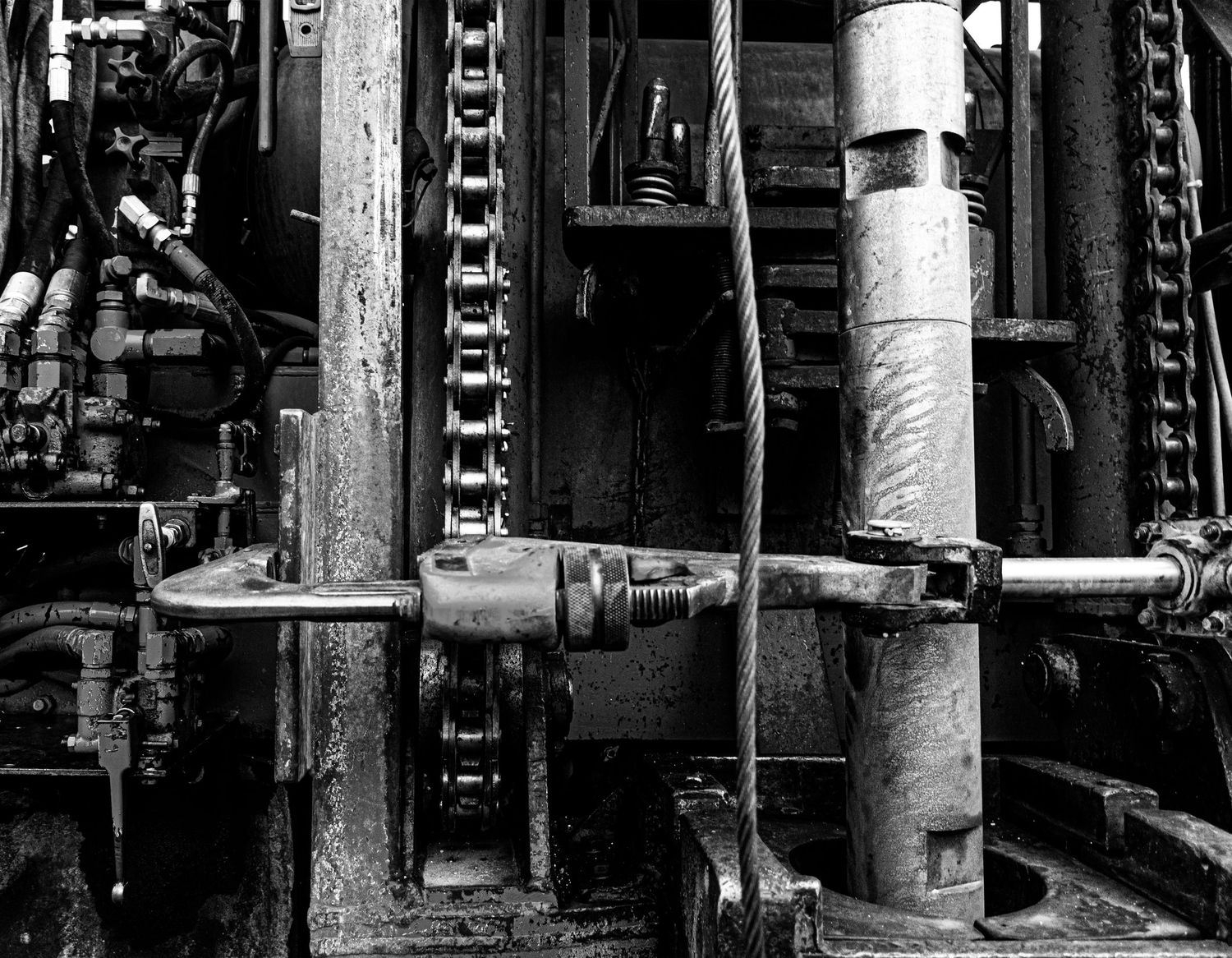 Close-up of industrial machinery showing metal pipes, chains and mechanical components in black and white.