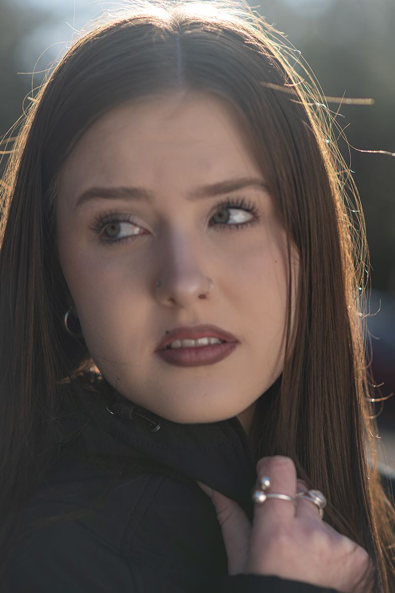Close-up portrait of someone with long dark hair and red lipstick against a backlit background.