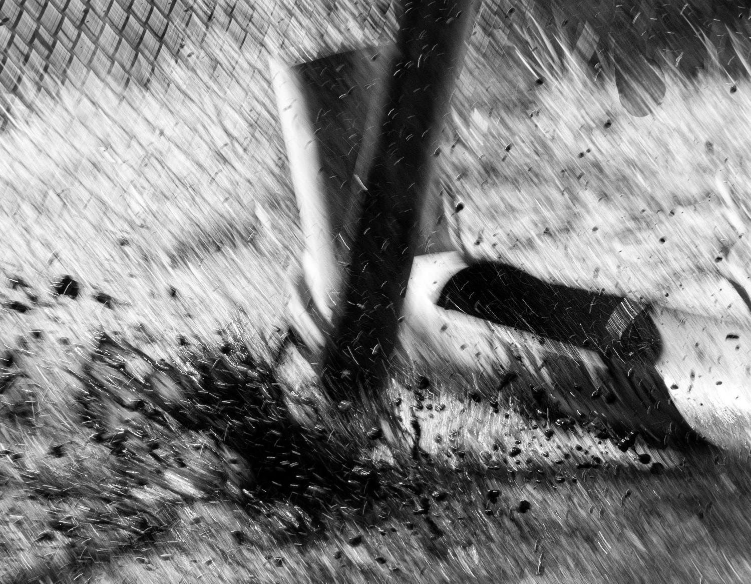 Dynamic black and white shot of a well drilling tool striking dirt with debris flying.