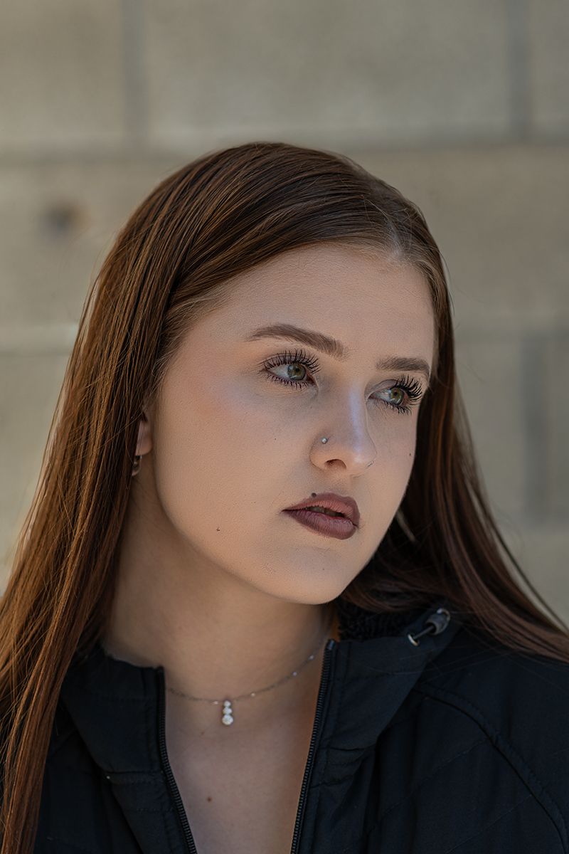 A person wearing dark lipstick and a black blazer poses for a dramatic portrait against a blurred background.