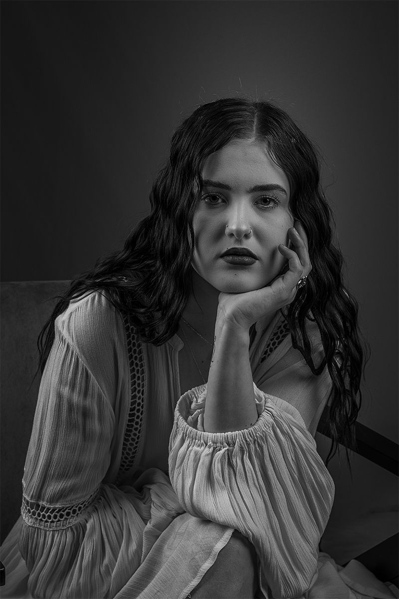 Black and white portrait of a person in a vintage-style white blouse with flowing sleeves resting their chin on their hand.