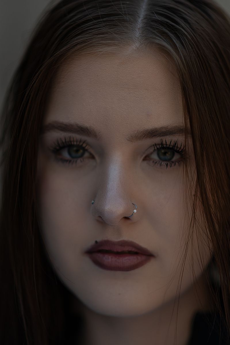 Close-up portrait with dramatic lighting showcasing dark red lipstick and blue eyes against a dark background.