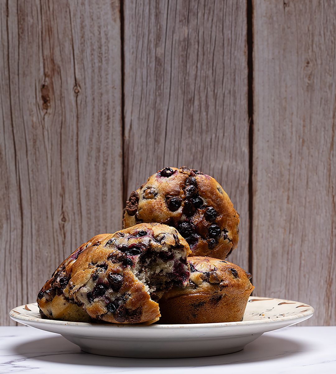 Fresh huckleberry muffins on a white plate against weathered wood background.
