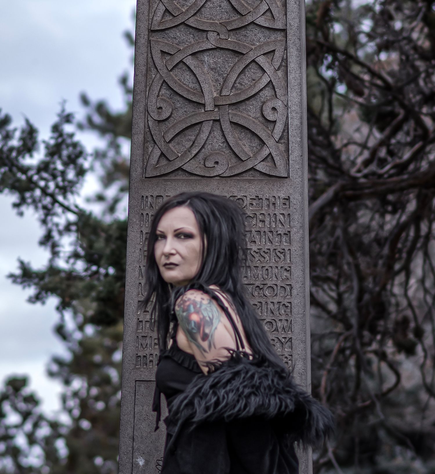 A gothic scene with carved stone cross artwork and dark attire against a moody sky background.