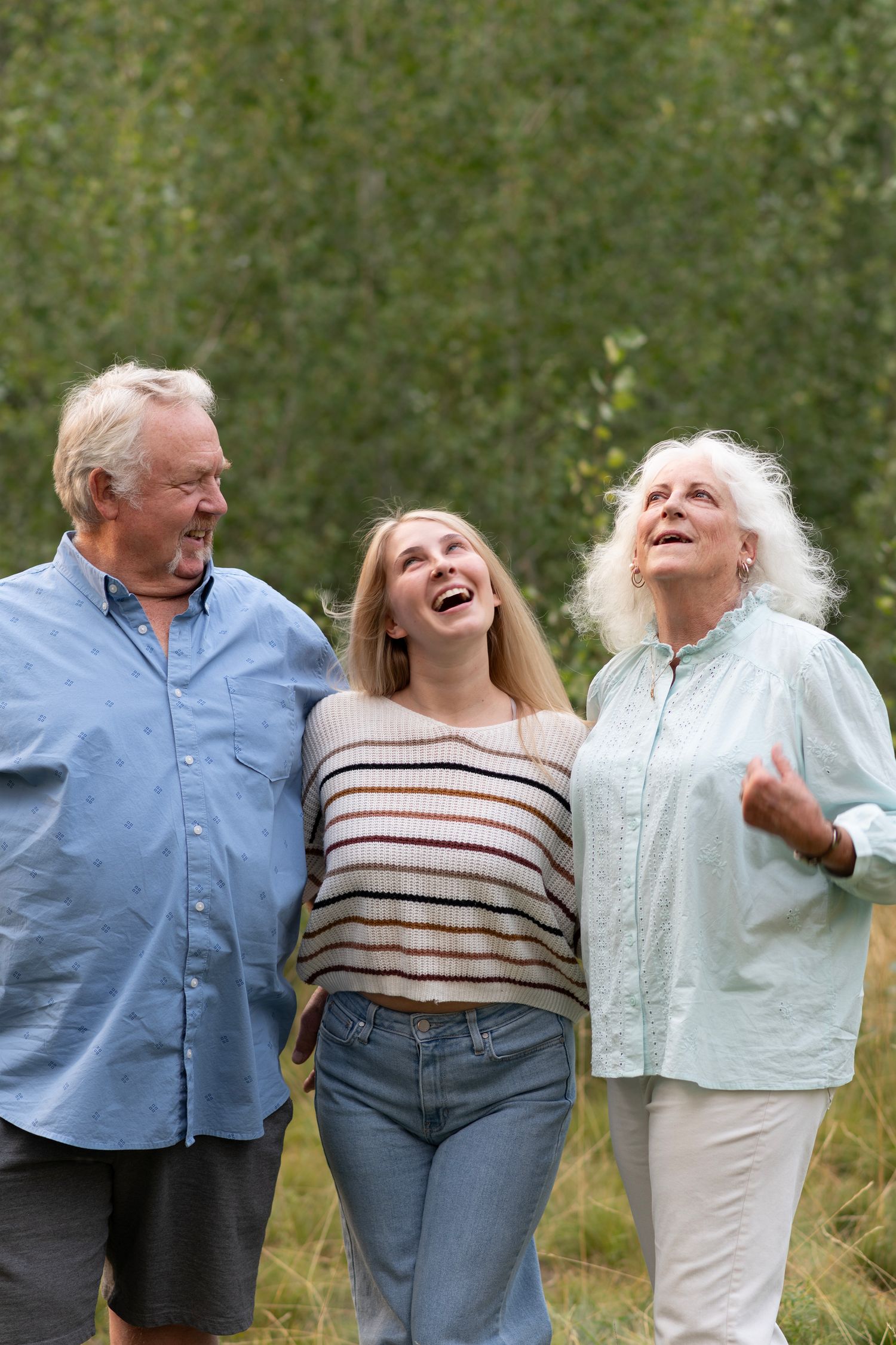 Three people laugh joyfully together outdoors in casual clothing on a sunny day.