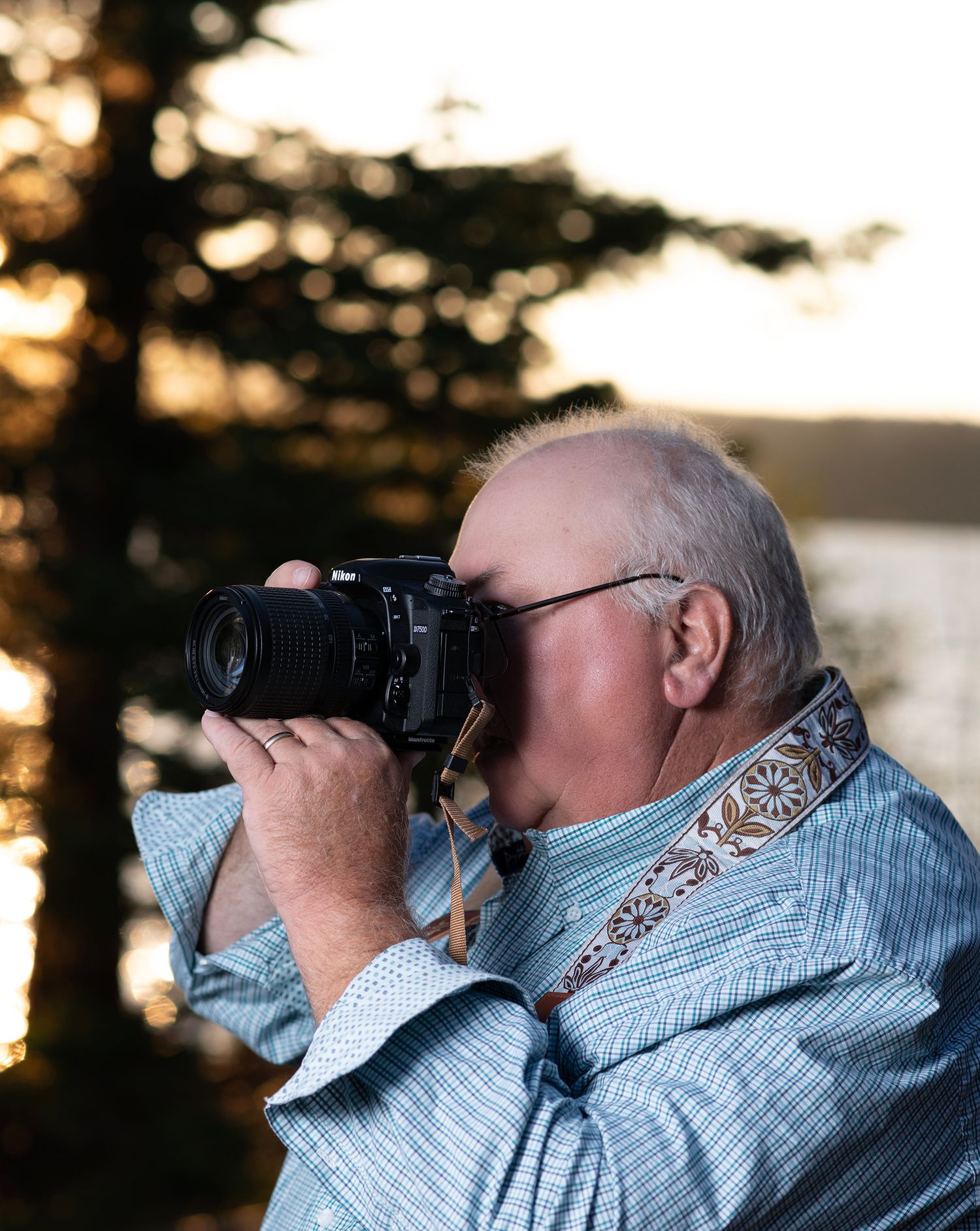 Person wearing a light blue jacket uses binoculars to gaze at nature during golden sunset hour.