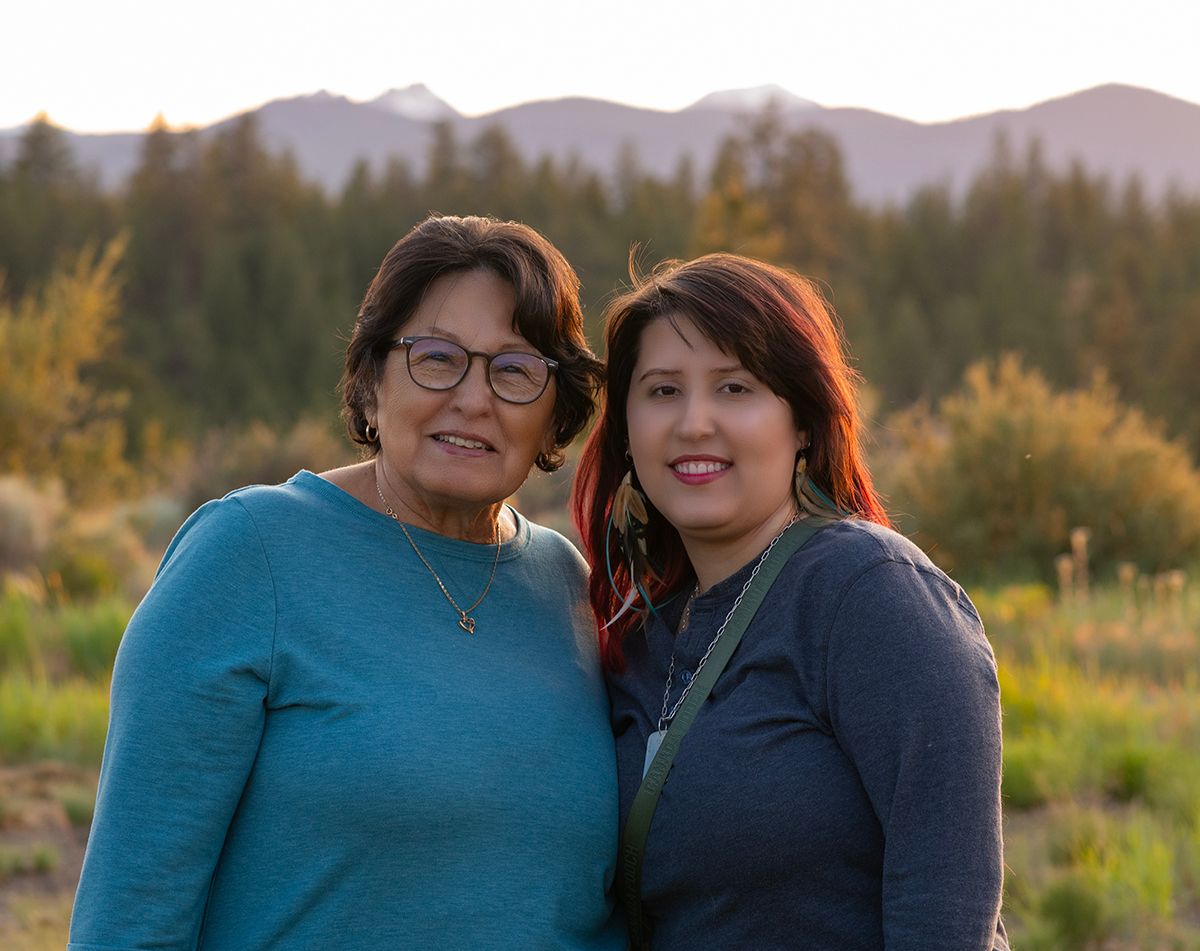 Grandmother and granddaughter sharing a close moment during golden hour with mountain landscape behind them.