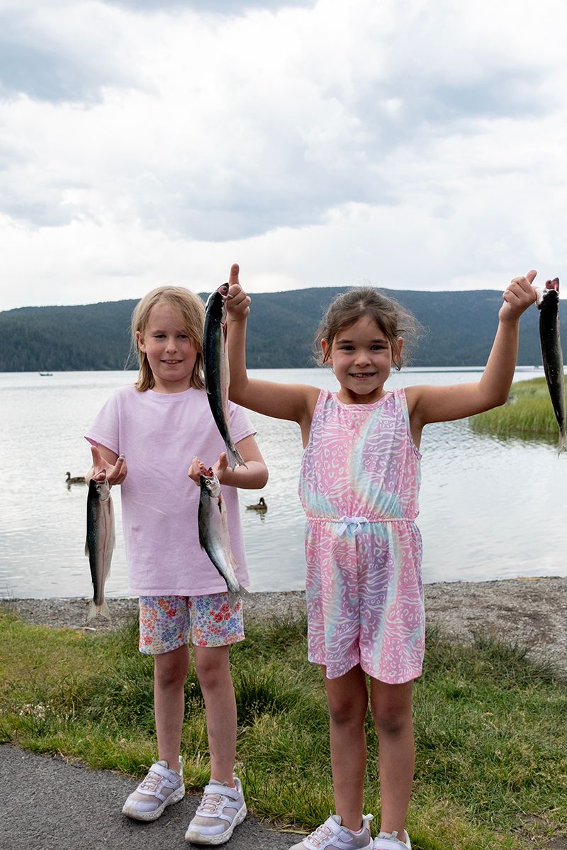 Two young children showing off their caught fish by a lake.