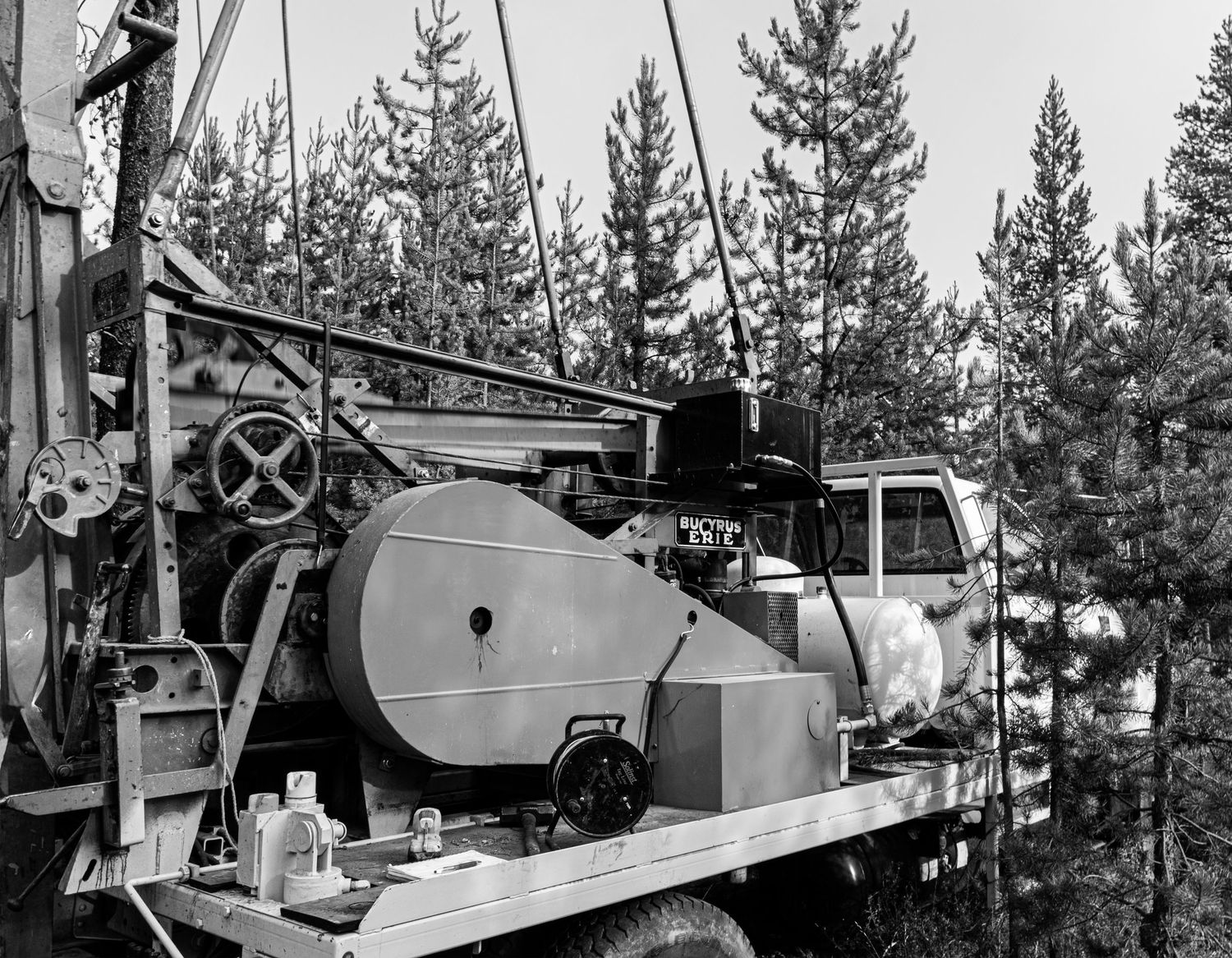 Historic black and white image of industrial drilling machinery mounted on a truck in a forest.