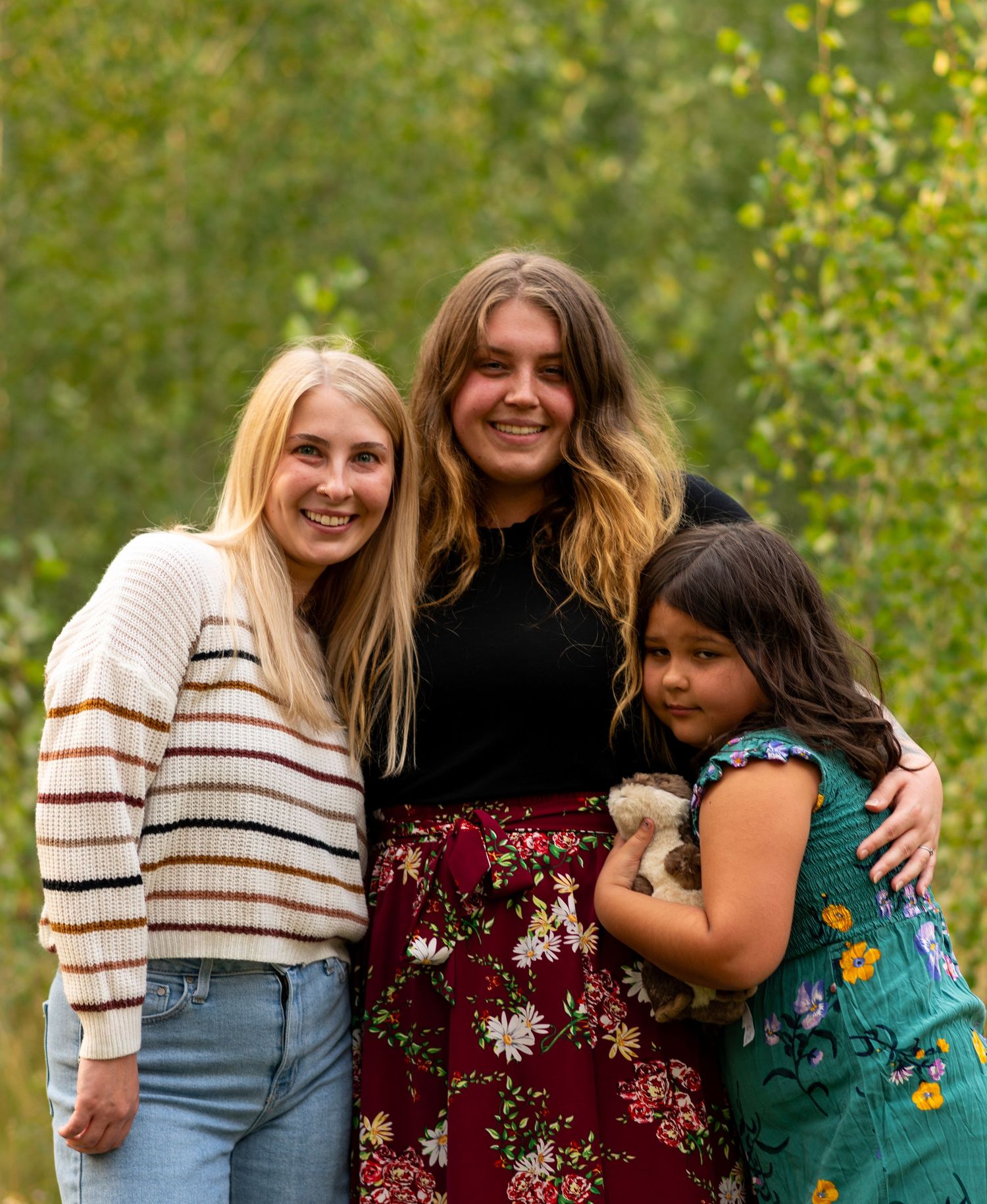 A sequence of candid outdoor photos showing three women embracing and sharing joyful moments in a natural setting.