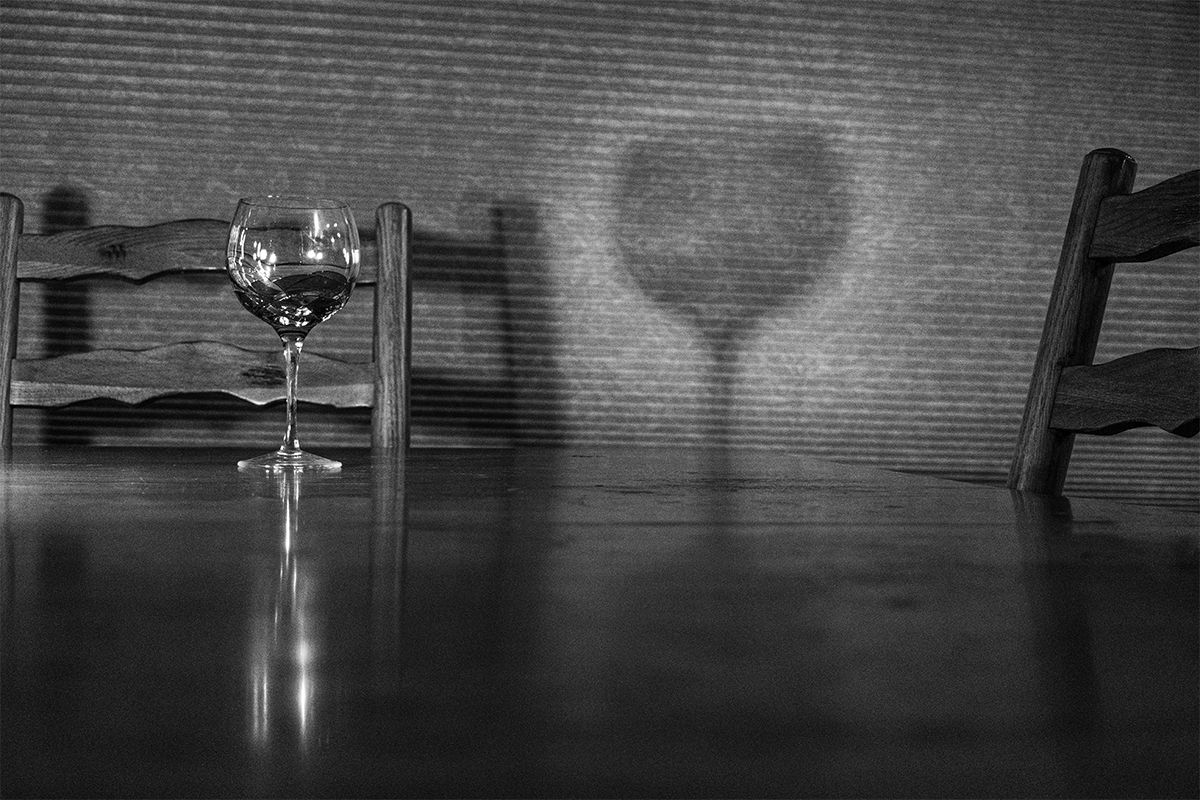 Wine glass on wooden table casting dramatic heart-shaped shadow in black and white.