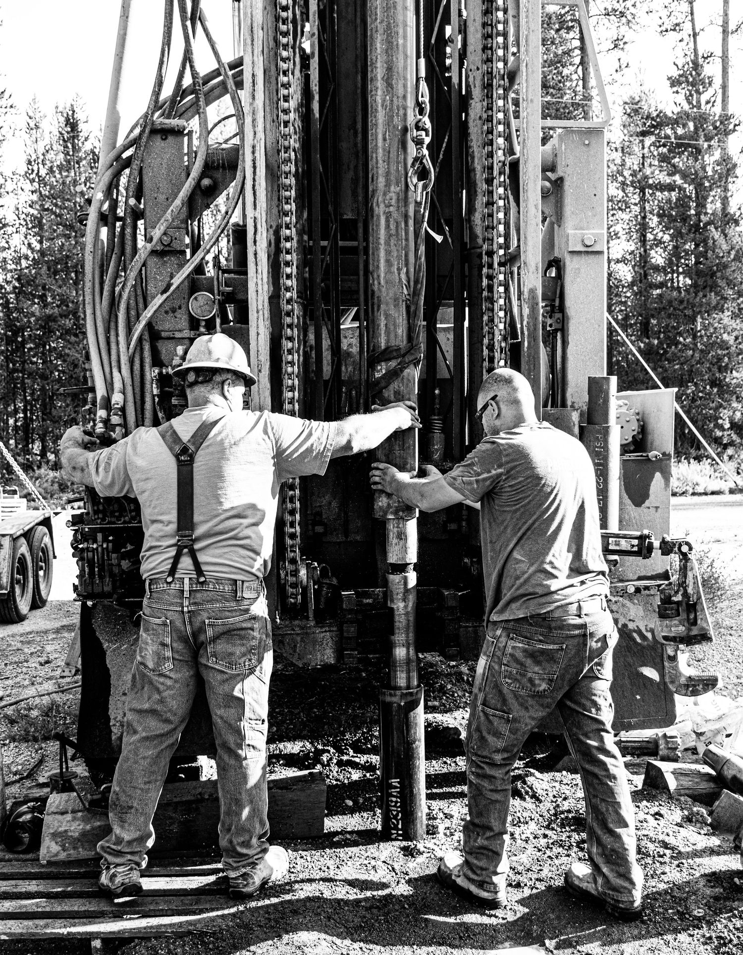 Workers operating heavy drilling equipment in a forested area wearing safety gear.