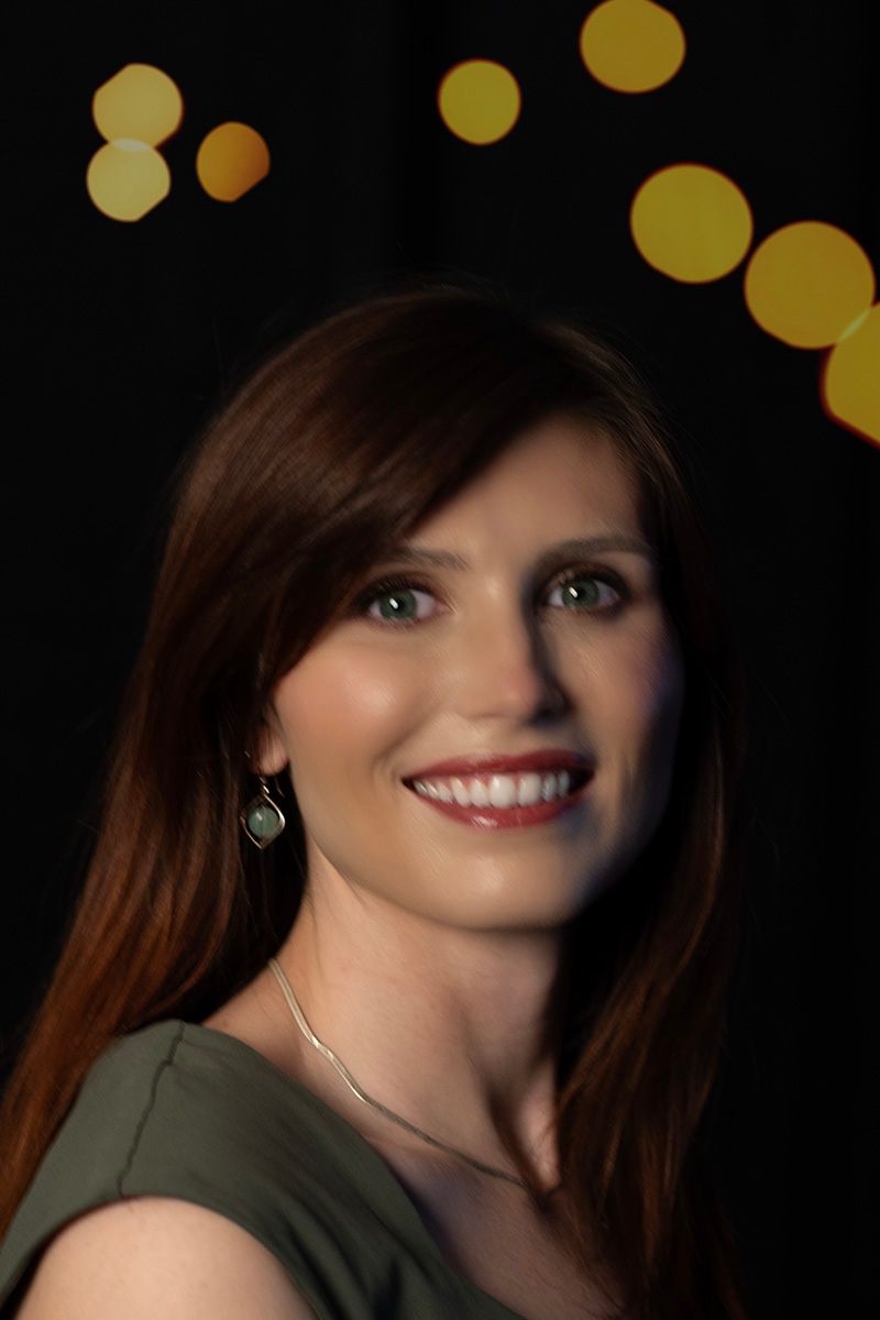 Portrait against dark background with golden bokeh lights and elegant jewelry.