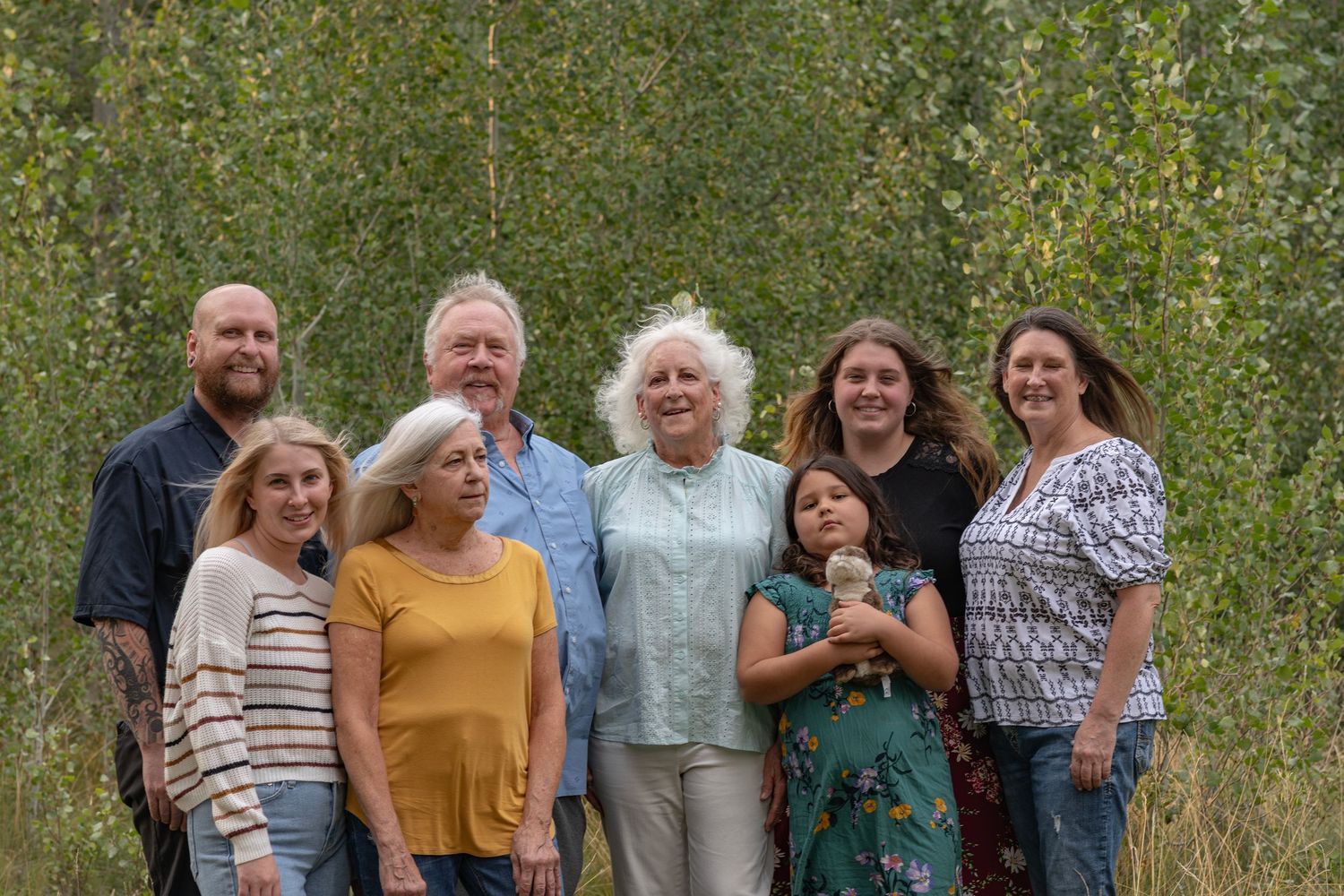 Outdoors family gathering photo with multiple people standing together in casual clothing against a natural backdrop.
