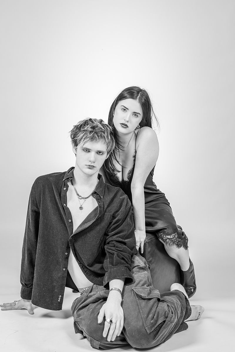 Black and white studio portrait of two people posing together in casual attire against a plain background.
