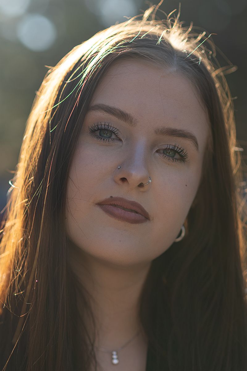 Portrait of a young woman in golden sunlight with long dark hair and mauve lipstick looking into the distance.
