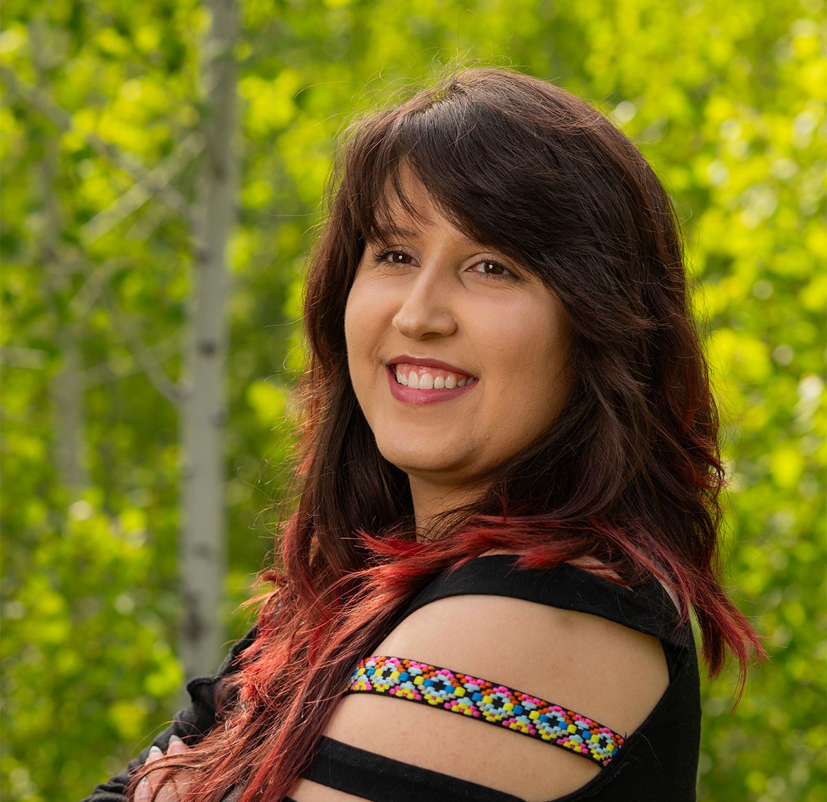 Portrait of someone with long dark hair outdoors against green foliage wearing tribal-inspired armband.