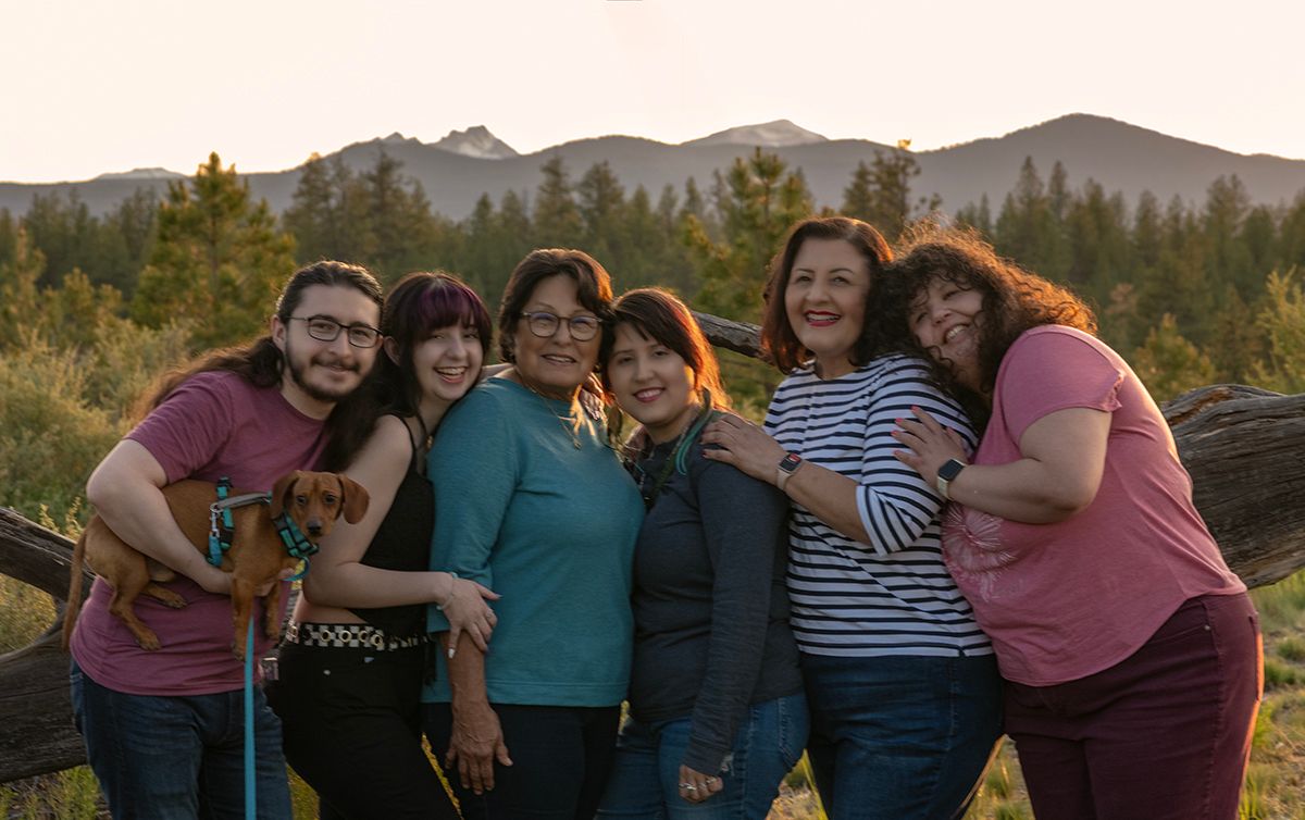 Family posing together outdoors with mountains and forest in the background at sunset.