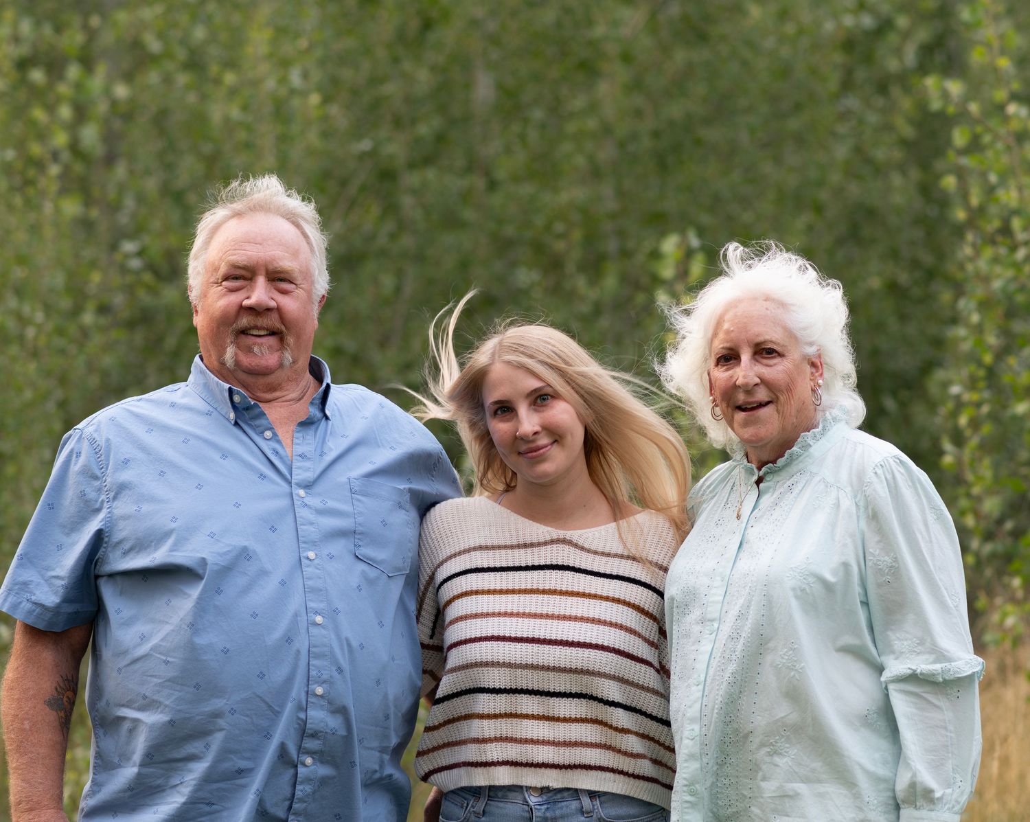 A group of people stand together outdoors in front of green foliage smiling and laughing.
