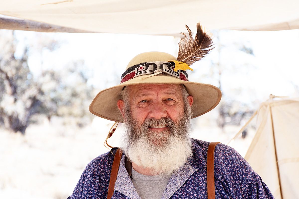 Person wearing a decorated hat with feathers and purple clothing outdoors on a sunny day.