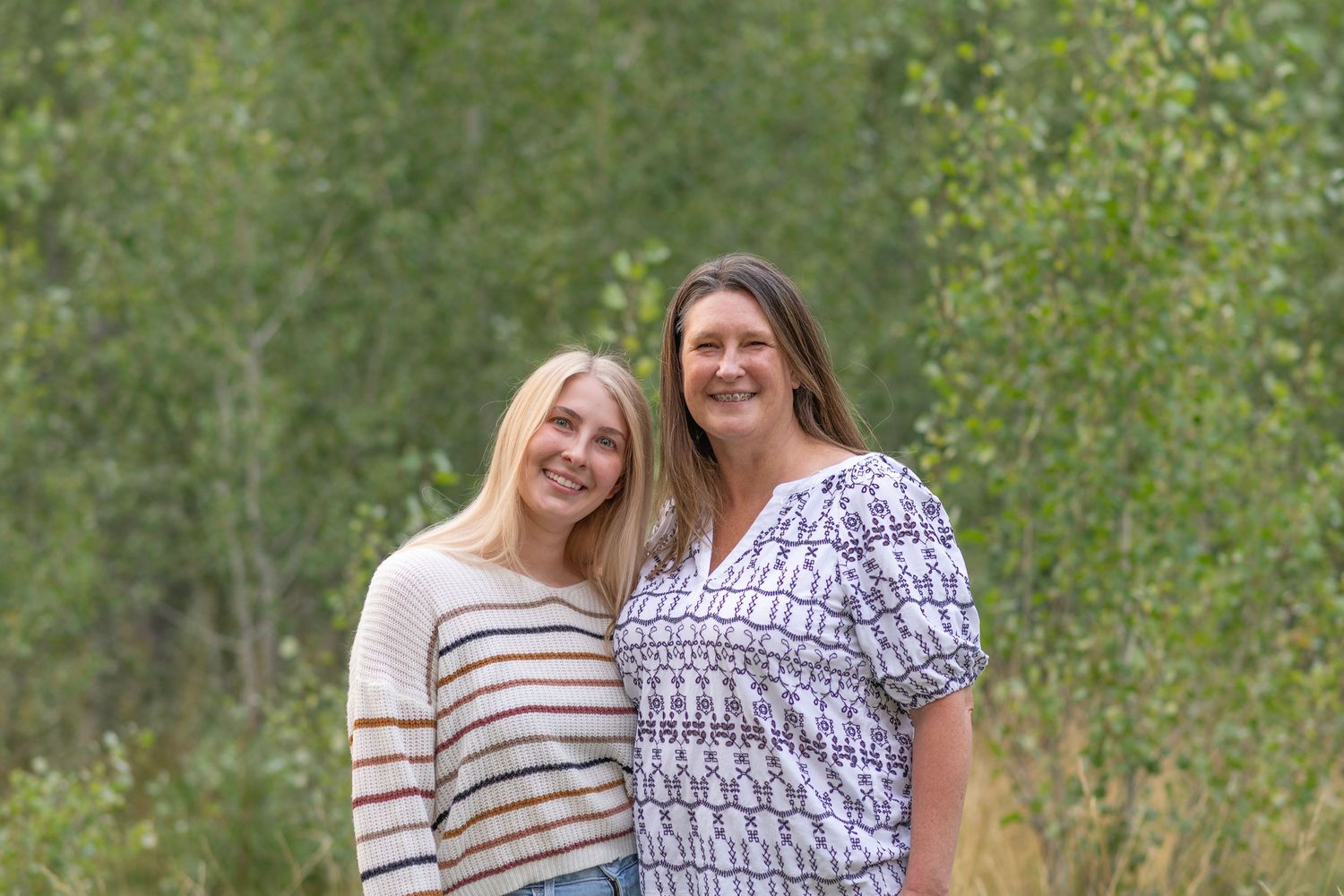 Two people in casual summer attire share a happy moment while standing together in a lush green outdoor setting.