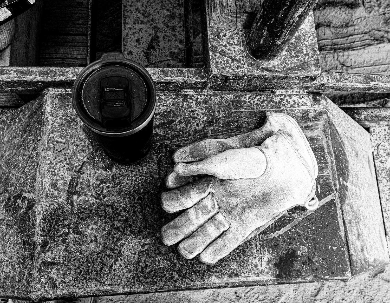 Dusty gloved hand resting next to a dark container on a workbench surface.