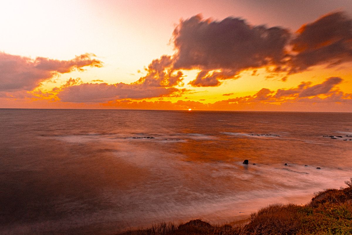 Dramatic orange sunset over a rugged coastline with dark clouds and waves crashing against the shore.