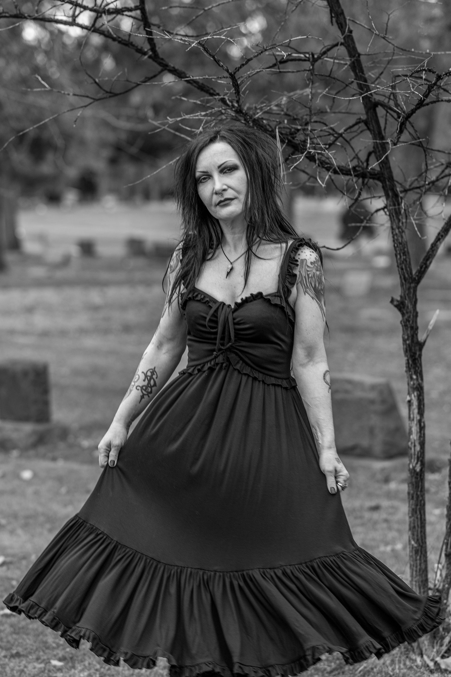 Dark romantic scene featuring flowing black dress against stark winter landscape with bare trees in background.