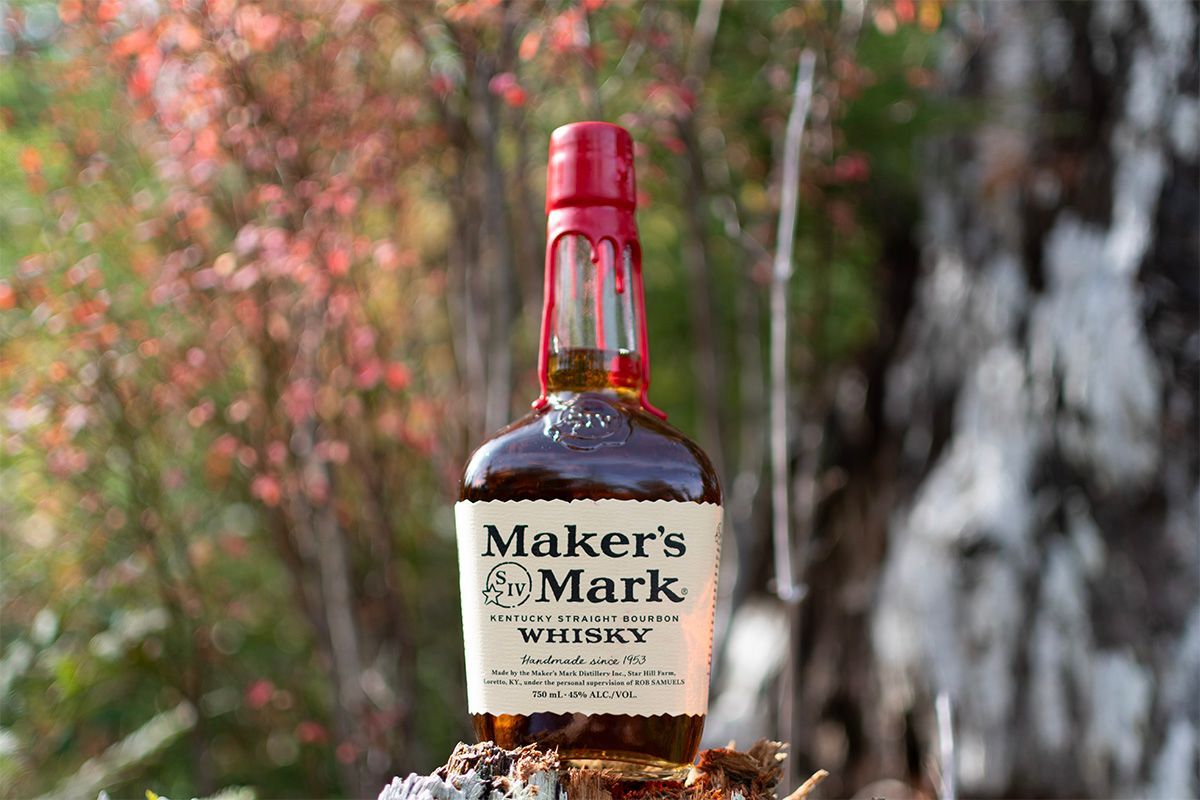 Bottle of Maker's Mark whiskey photographed outdoors with autumn foliage in background.