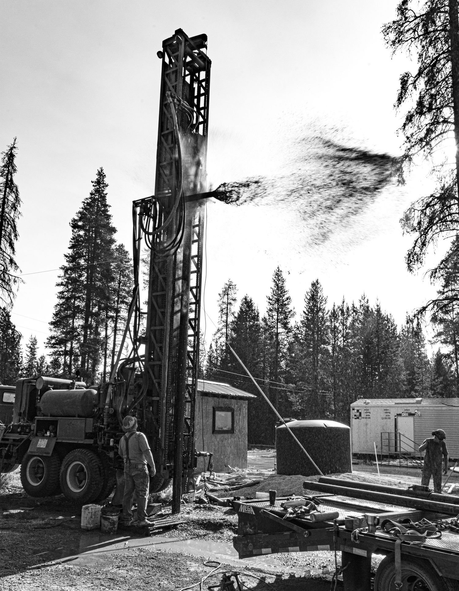 Vintage black and white photo of industrial drilling equipment at a forest work site.