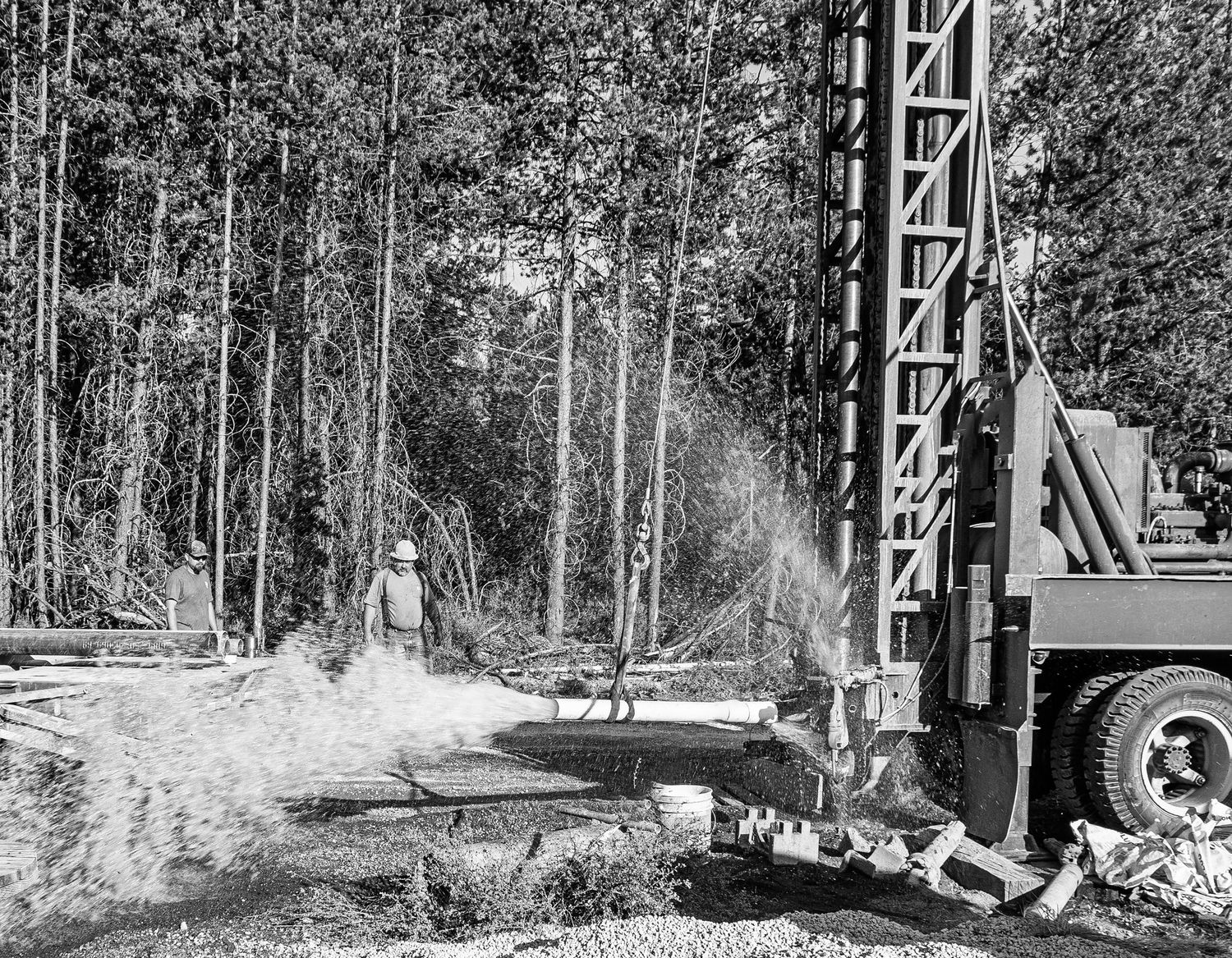 Industrial drilling equipment operating in a wooded area creating dust clouds.