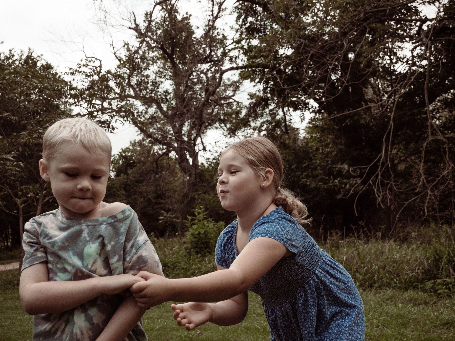 Two children play and interact together outdoors in a natural wooded setting.