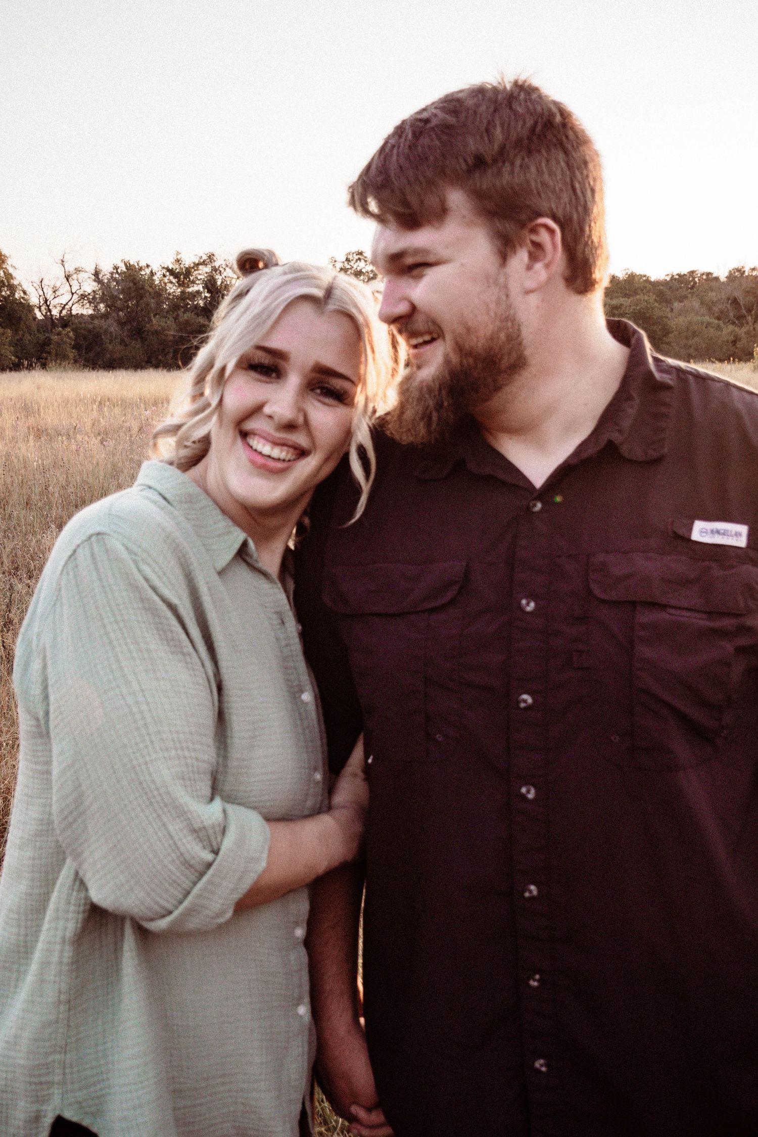 Happy couple shares a candid moment together in field during golden hour.