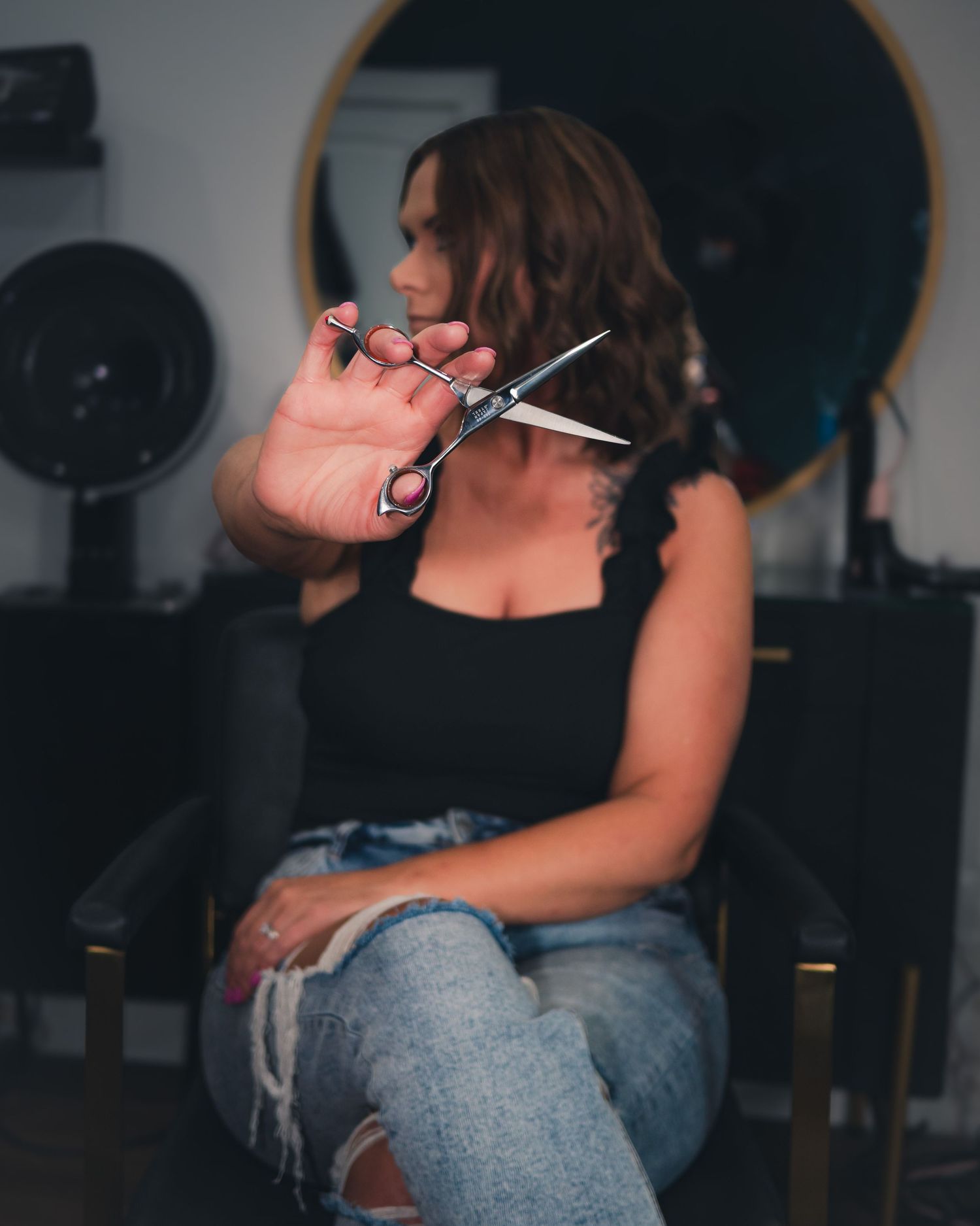Person holding scissors out in front of them in a dimly lit salon with a round mirror.