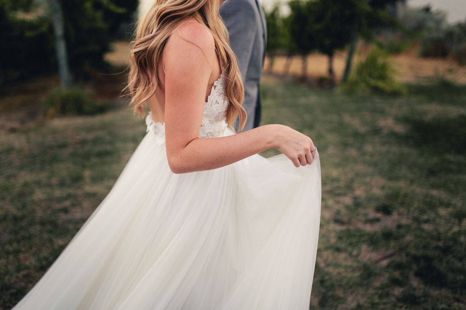 Detail shot of a flowing white tulle wedding dress being held in natural lighting.