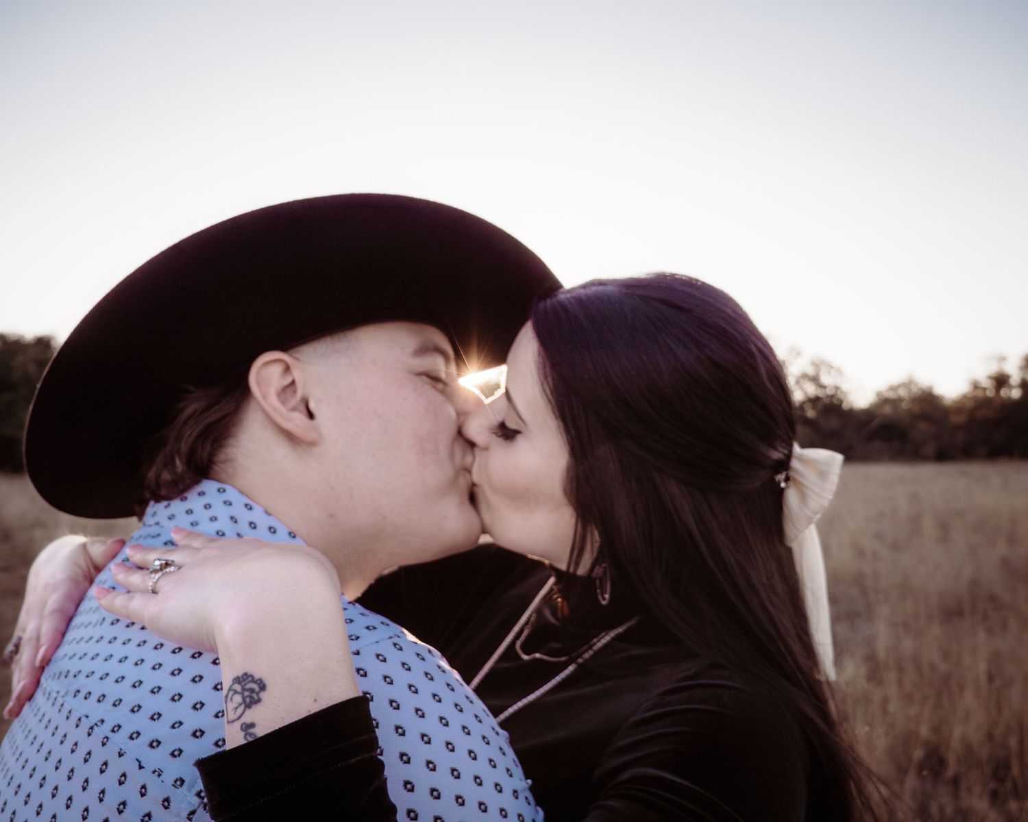 A romantic kiss shared in a golden field with one person wearing a cowboy hat.