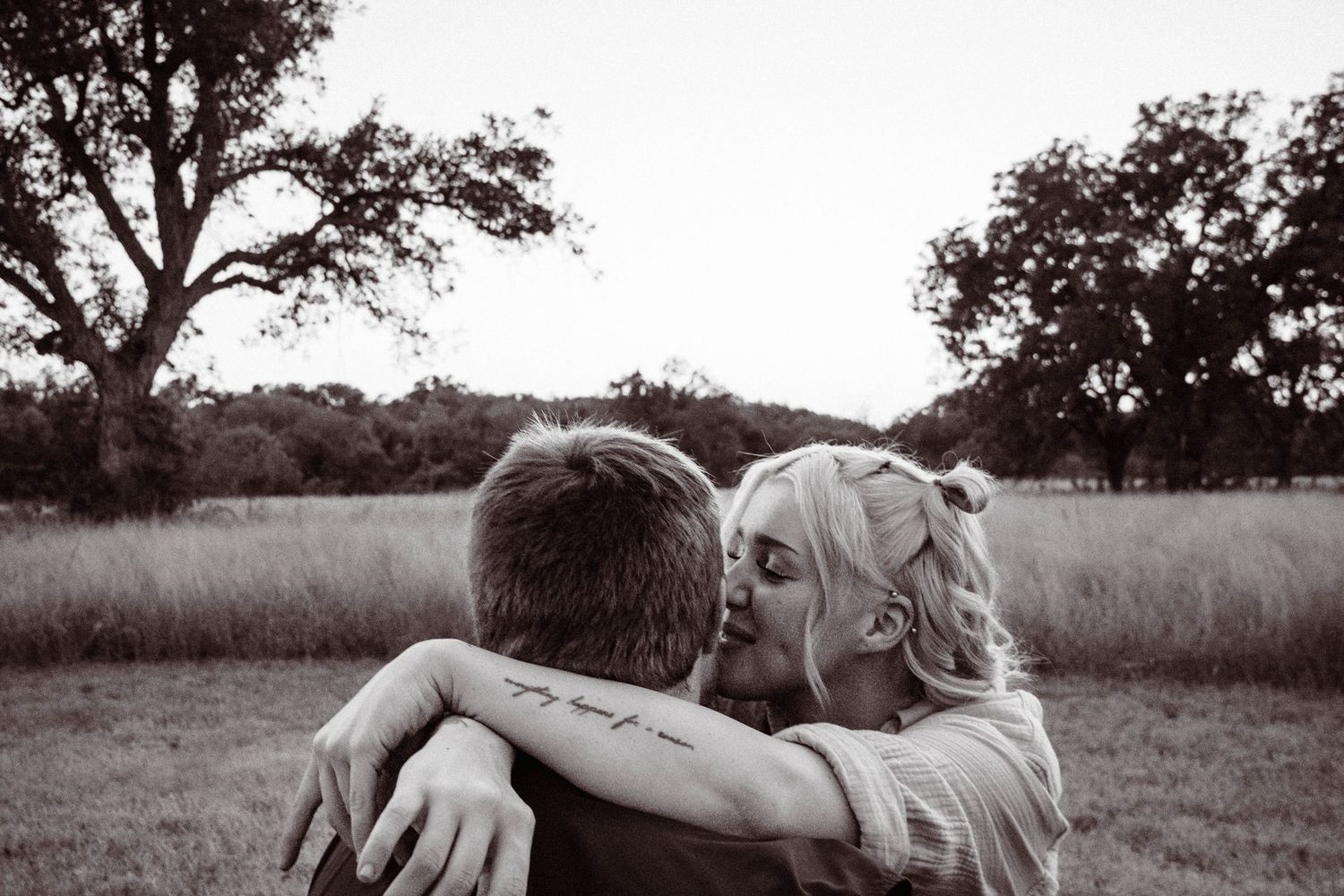 A romantic black and white countryside scene showing an intimate moment between a couple in a grassy field.
