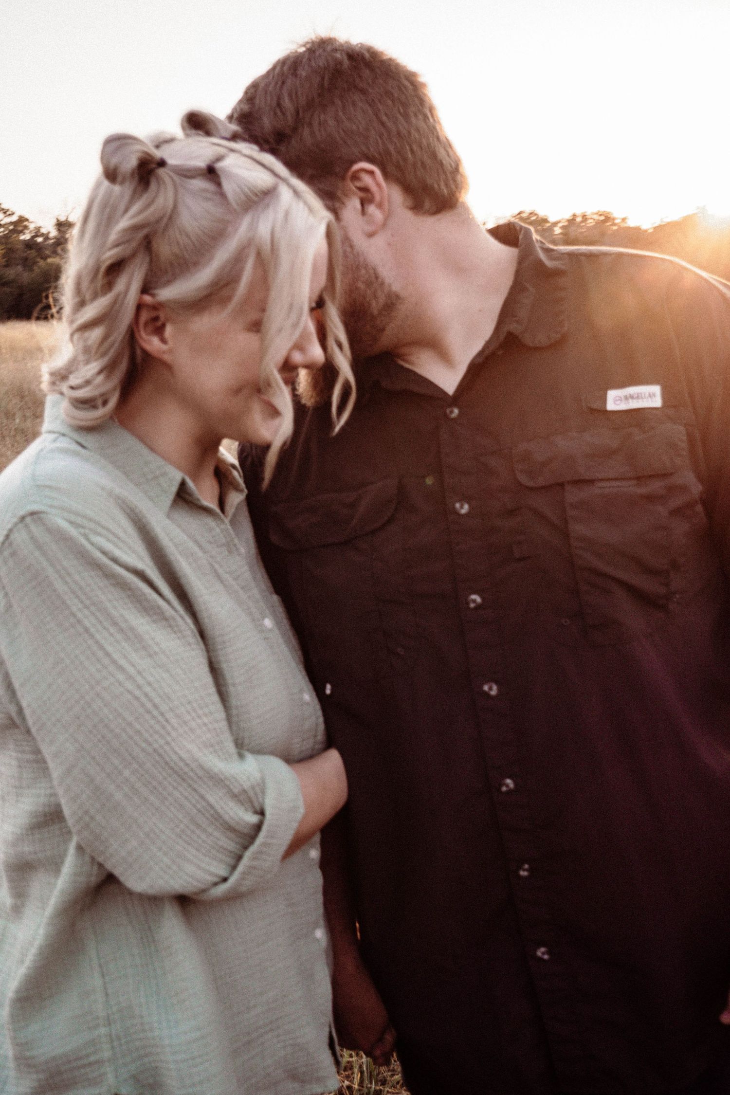 A romantic couple shares an intimate moment at sunset in a field, with warm golden light behind them.