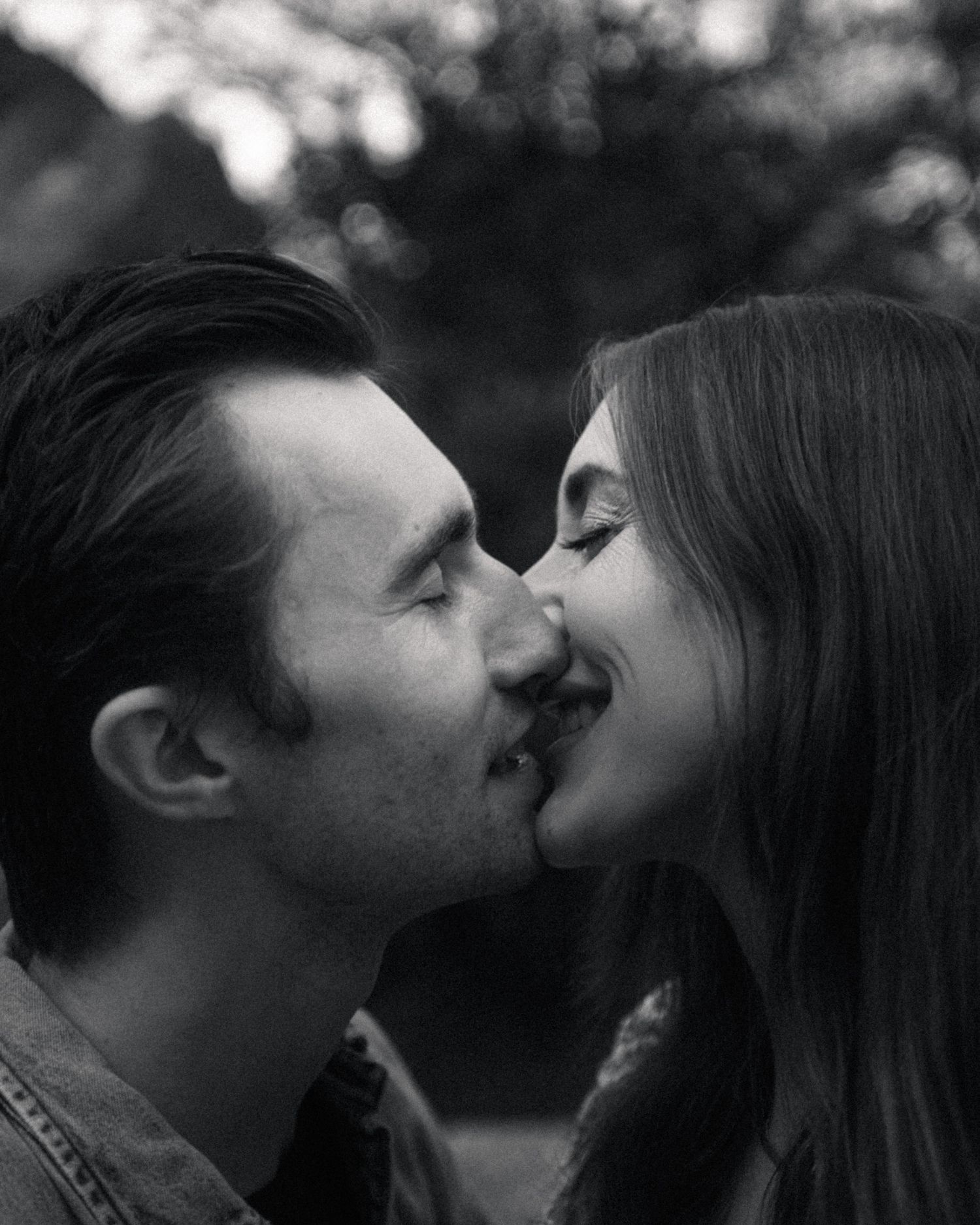 A romantic black and white portrait shows a close-up of a couple sharing an intimate kiss outdoors.