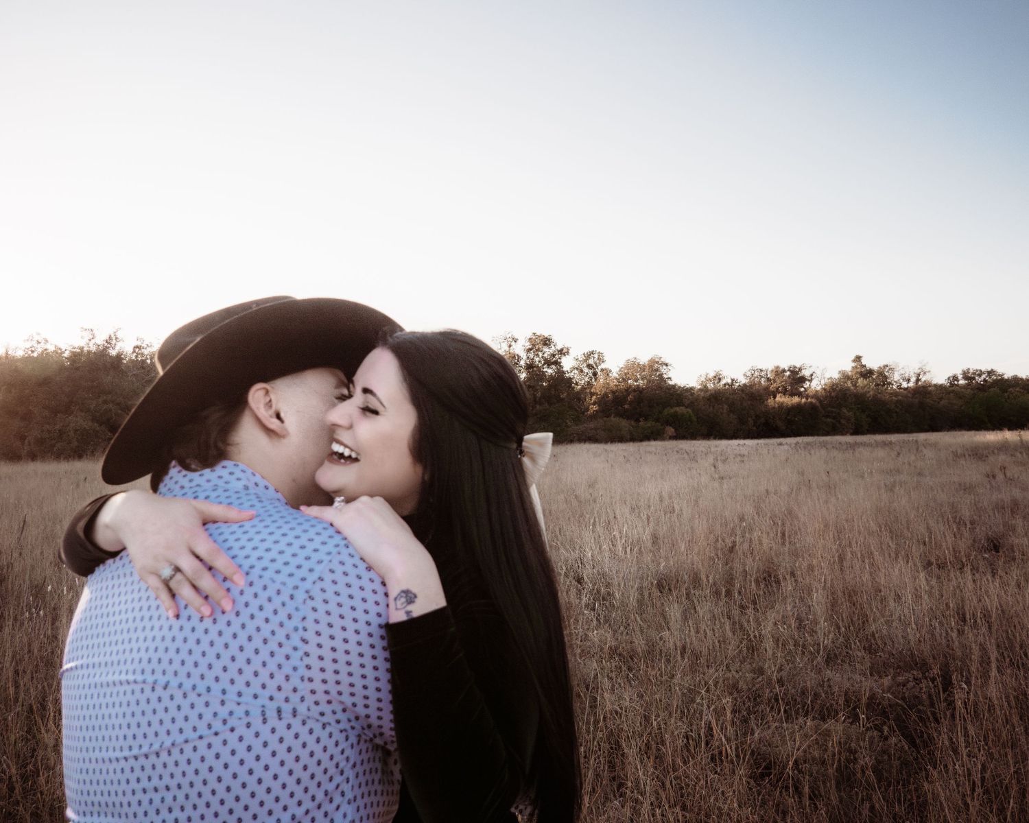 A couple embraces in a romantic moment against a golden sunset in a grassy field.