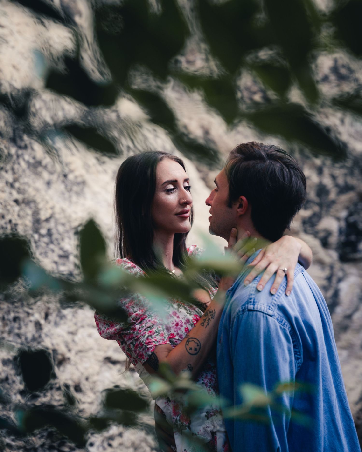 A romantic couple in blue and floral attire sharing intimate moments against a blurred nature backdrop.