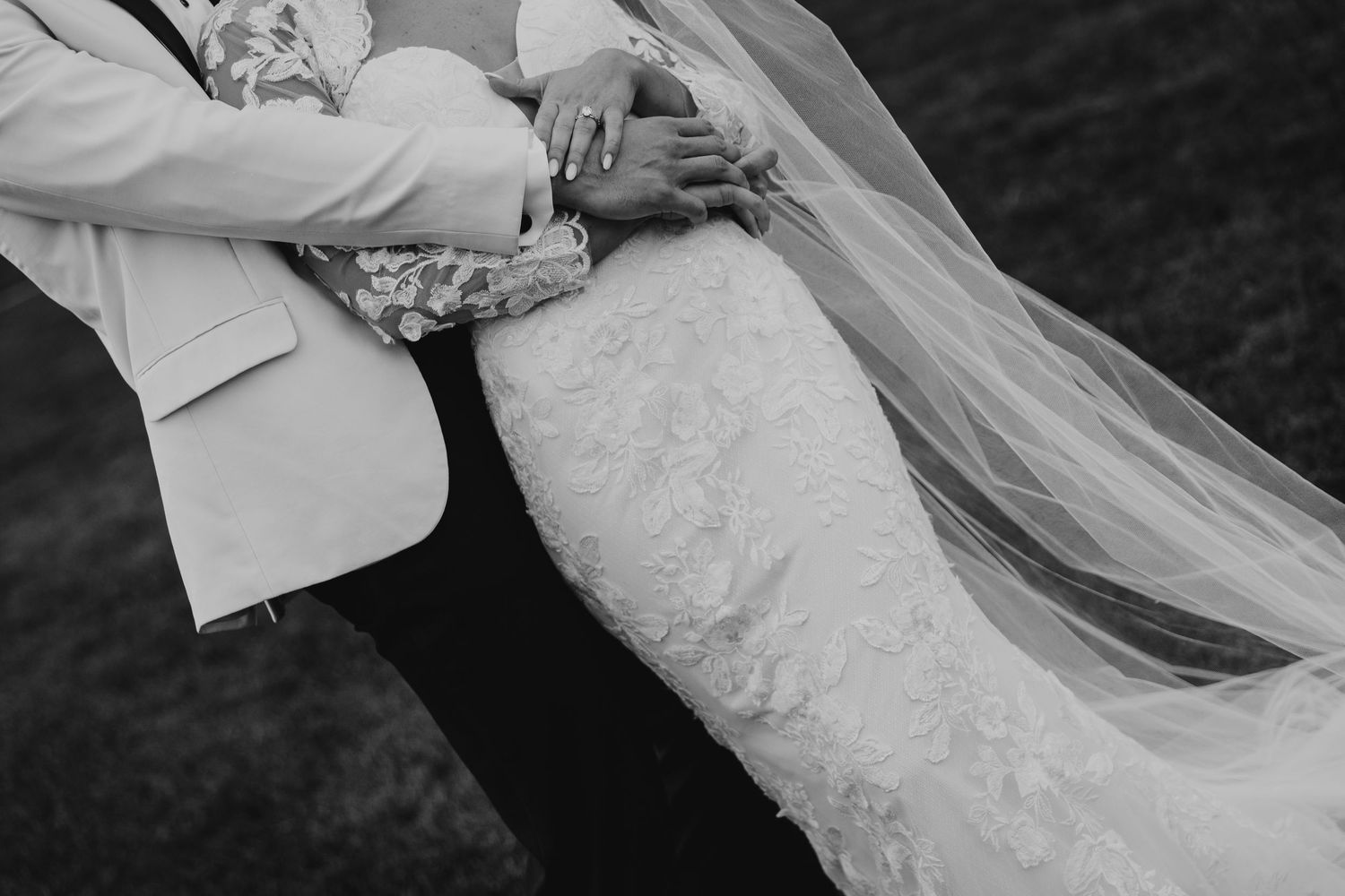 A bride and groom share a romantic kiss while her veil flows in the wind during an outdoor wedding ceremony.